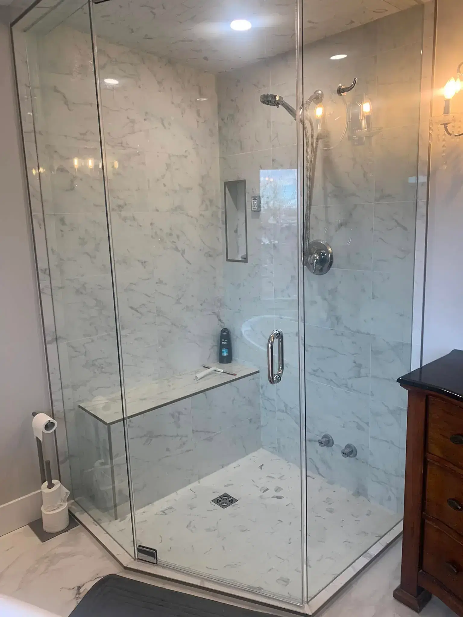 Corner frameless glass shower with marble-look tile, built-in bench seat, recessed niche, and chrome fixtures in Calgary