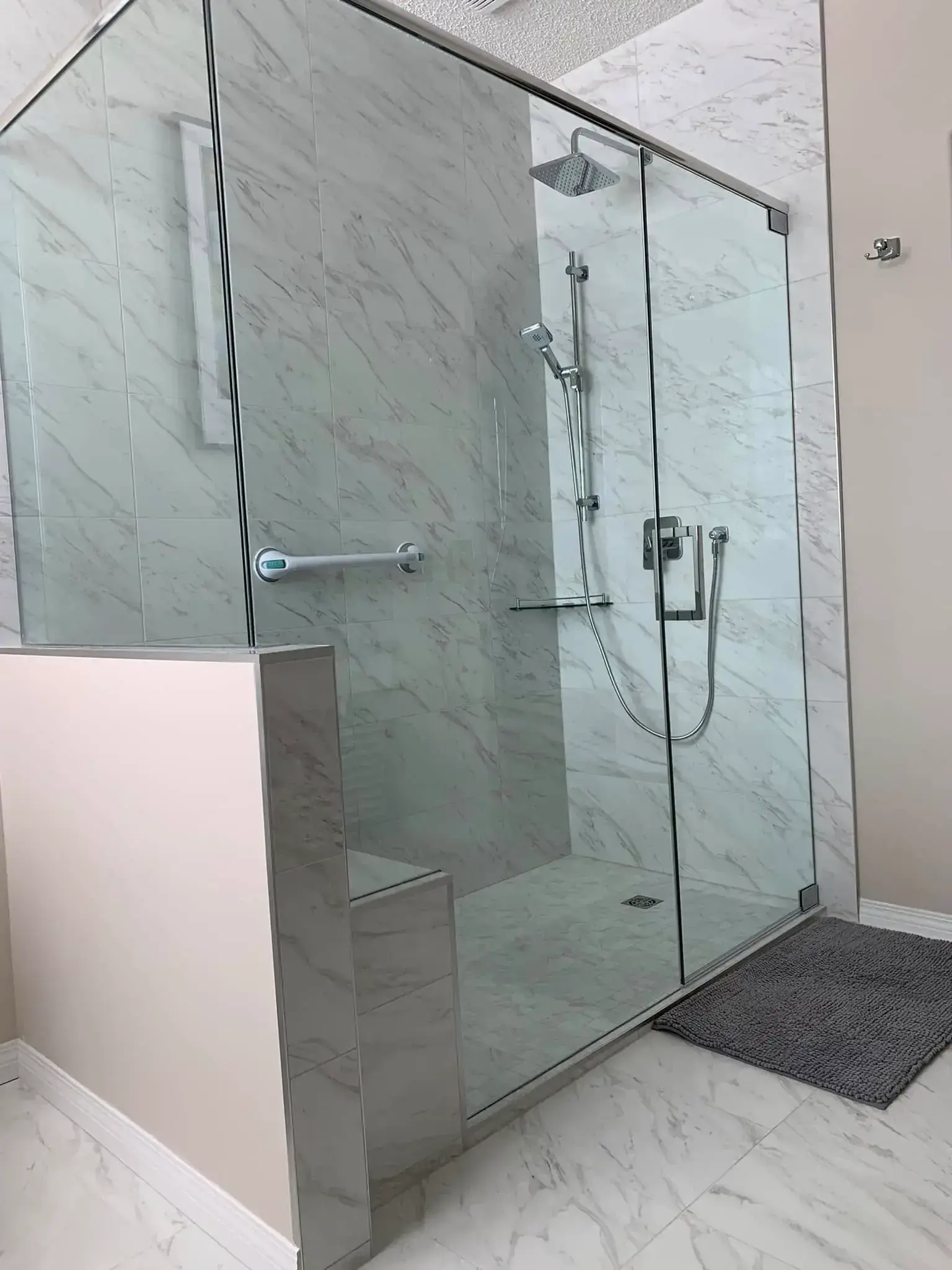 Large walk-in shower with marble tile, built-in bench, grab bar, and square rainfall showerhead in Calgary bathroom