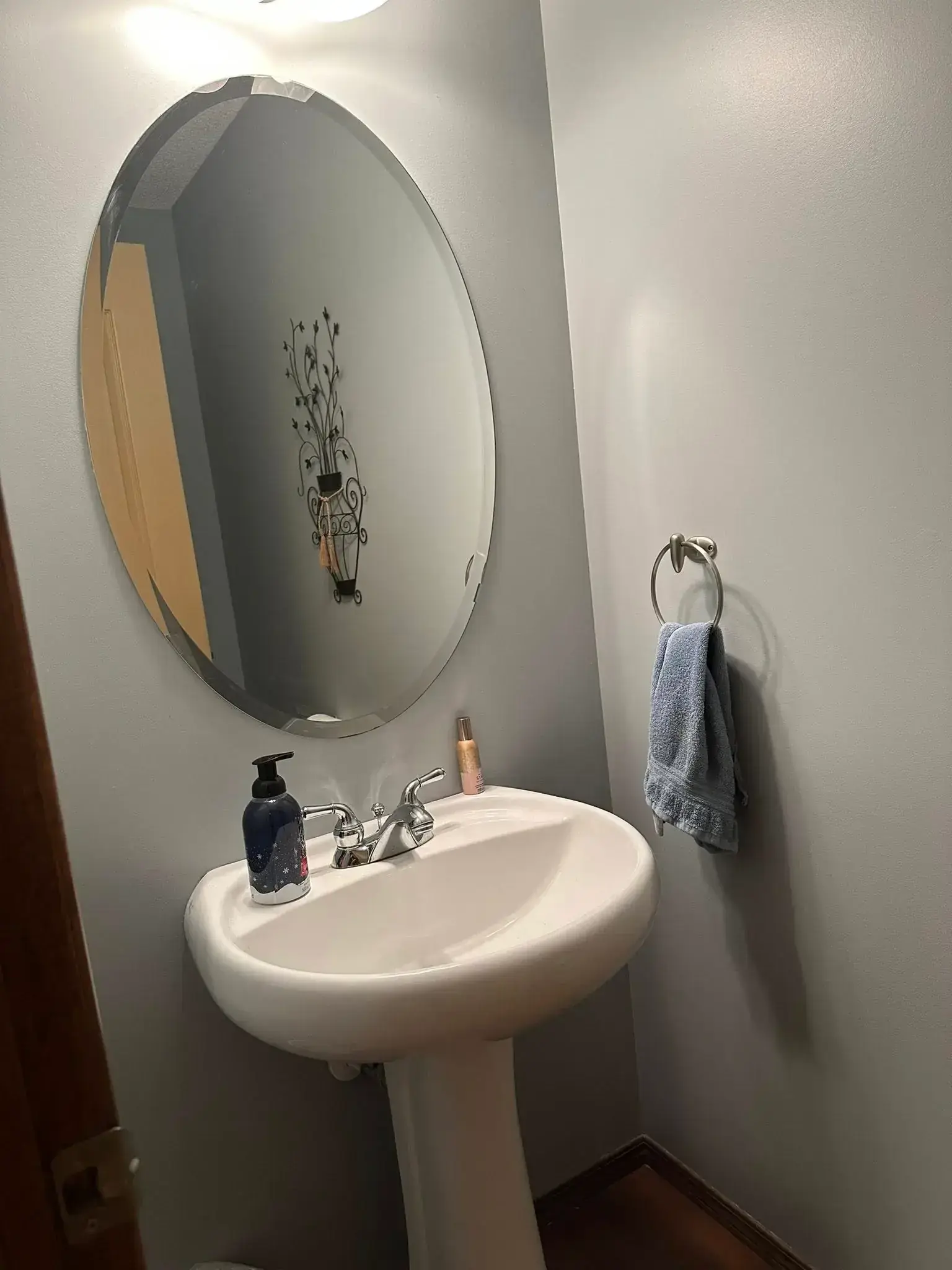 Renovated powder room with white pedestal sink, beveled oval mirror, chrome fixtures, and towel ring in Calgary home
