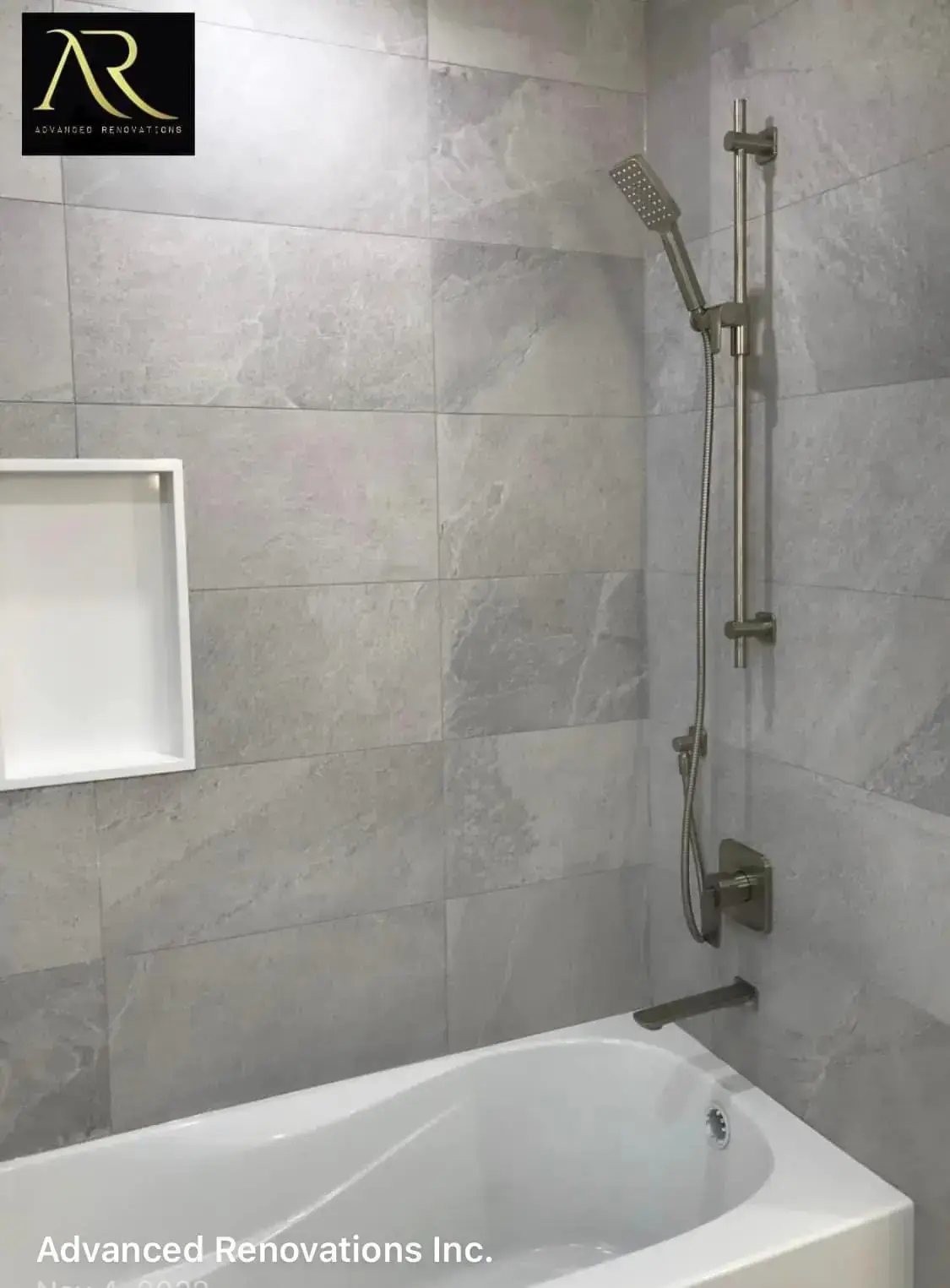Tub-shower combo with grey stone-look tile, recessed wall niche, and adjustable handheld shower in Calgary home