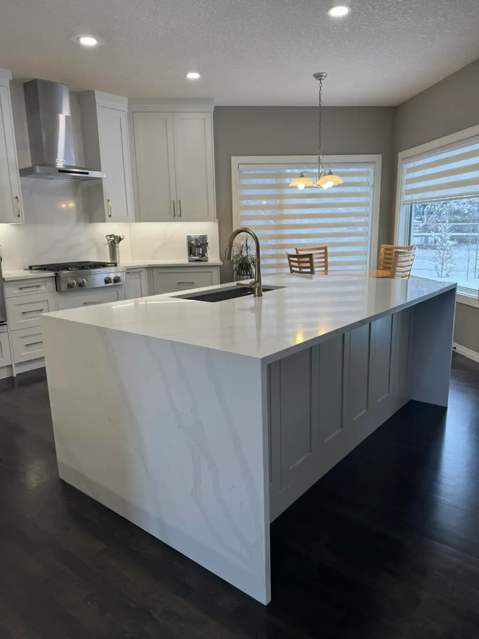 Modern kitchen renovation with white quartz waterfall island, light grey shaker cabinets, and dark hardwood floors in Calgary