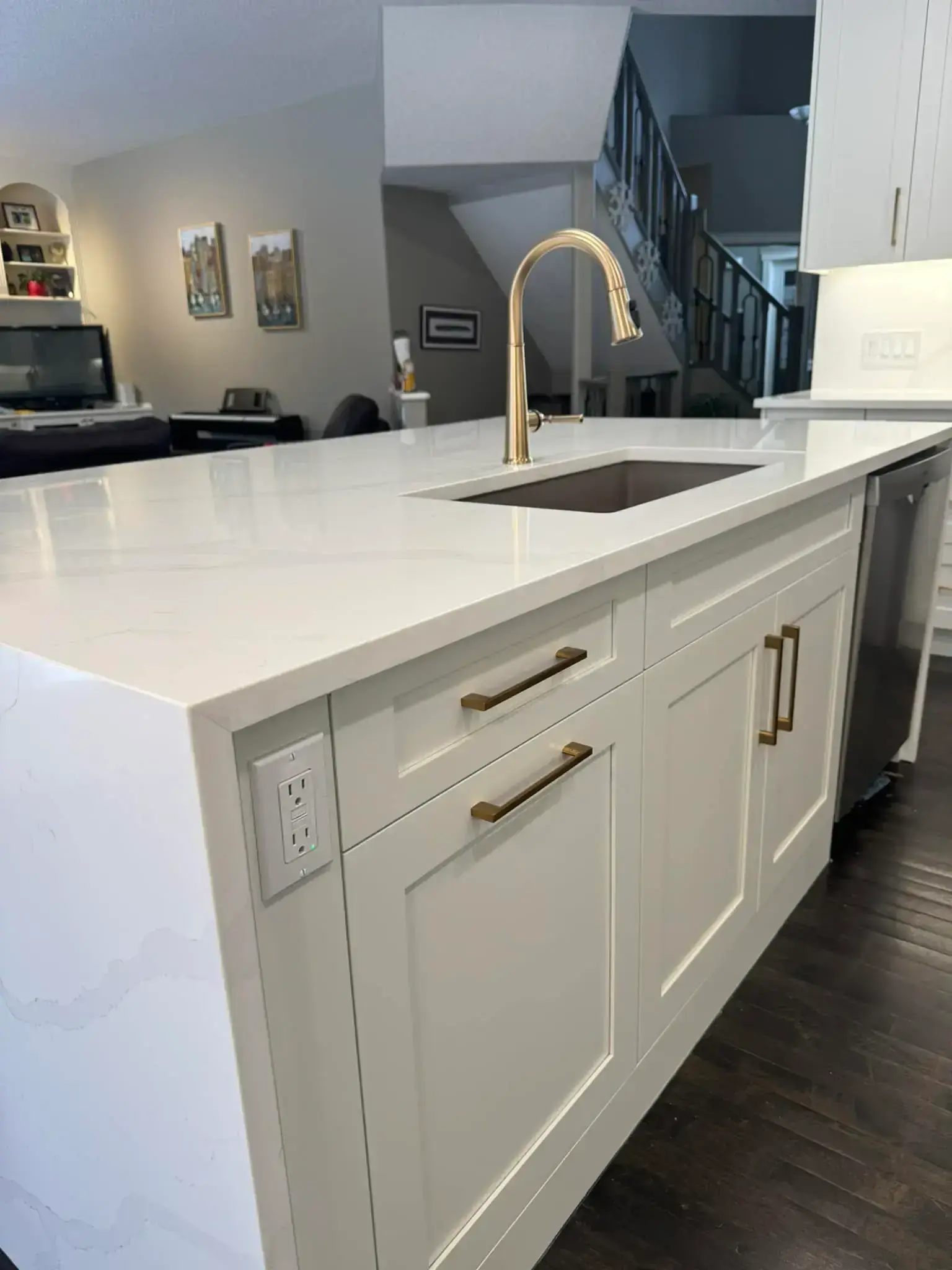 White shaker kitchen island with quartz waterfall countertop, gold faucet and hardware, and dark hardwood flooring in Calgary home